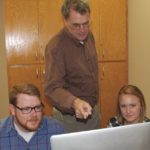 Hughes teaching two students in front of a computer