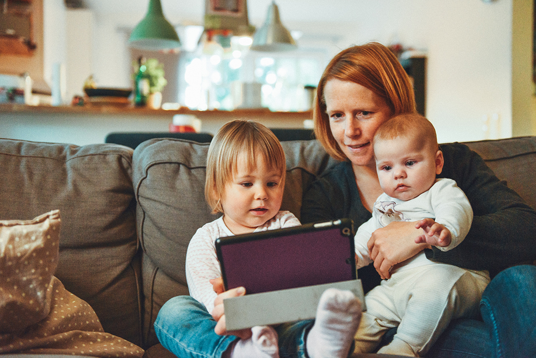 Picture of woman holding two children, reviewing information on a smart device