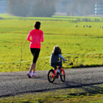 Picture of a woman running next to a child biking