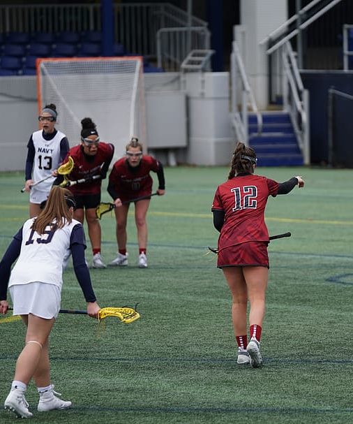 female lacrosse players play on a turf field 