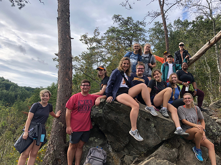 A group of students pose on a rock along a mountain trail
