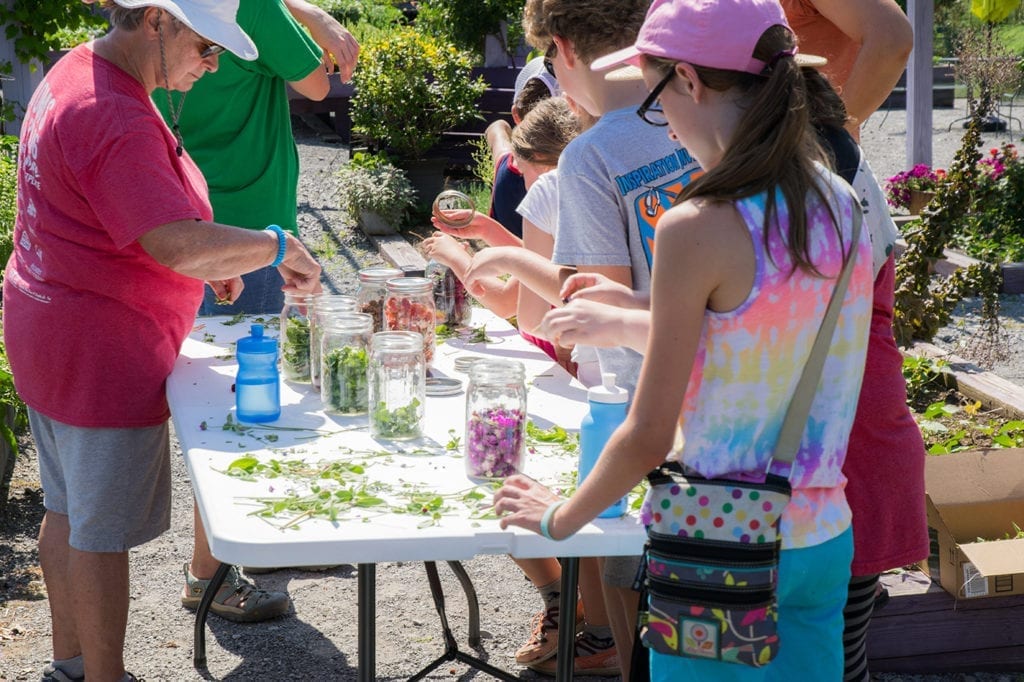 Children gathered around a table putting brightly colored flowers into jars