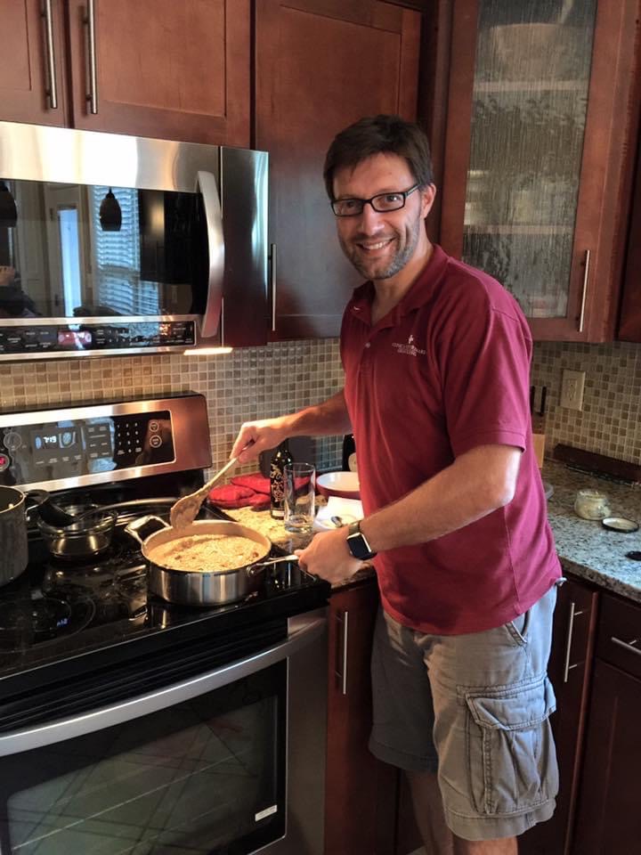 Luca Giori stands beside a stove with a pot of risotto and a wooden spoon